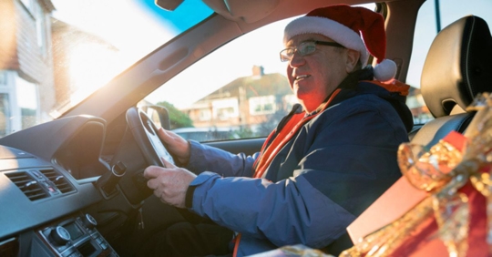 man in Santa hat driving with presents in car
